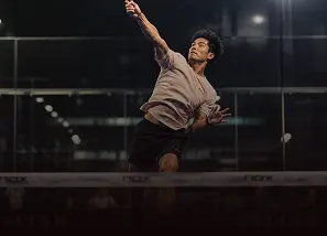 Pemain padel melompat melakukan smash overhead di lapangan indoor